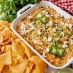 Street corn dip in a white baking dish next to tortilla chips and corn chips.