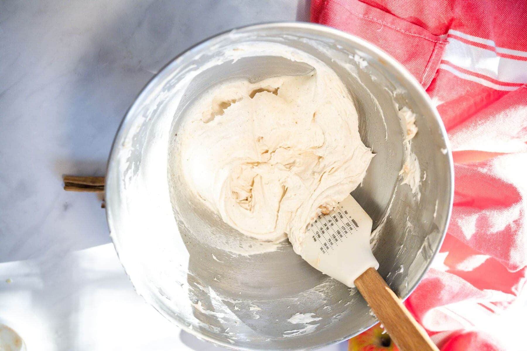 Cream cheese frosting mixed in bowl with spatula.