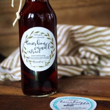 A bottle with dark liquid in it with label that reads; "Bourbon Vanilla Extract" with other label on the cutting board.