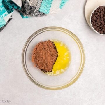 A glass bowl with melted butter and cocoa powder with a bowl of chocolate chips.