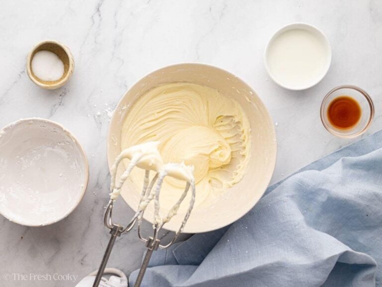 A white bowl with beaten cream cheese frosting and a hand mixer.