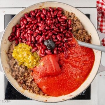 Beens, green chiles, tomato sauce added to the ground beef in a skillet.