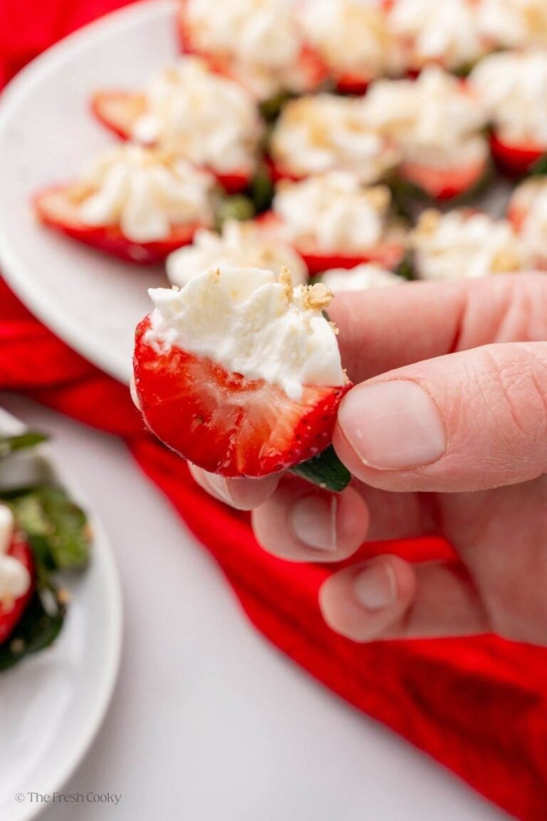 Hand holding a deviled strawberry with a bite taken out of it with more strawberries in the background.