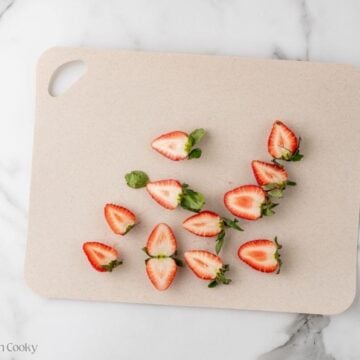 Strawberries sliced in half on a cutting board.