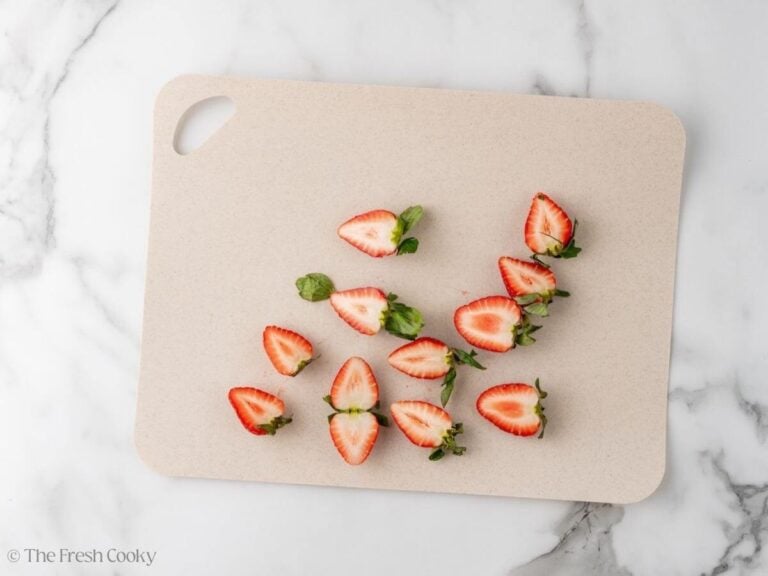 Strawberries sliced in half on a cutting board.