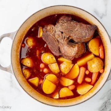 A Dutch oven with a chuck roast, potatoes, and carrots in broth and red wine.