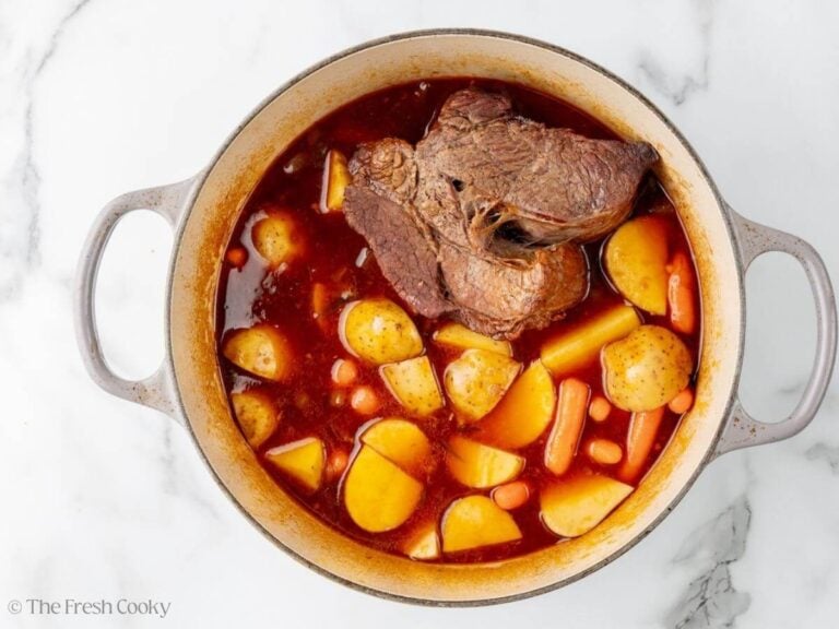 A Dutch oven with a chuck roast, potatoes, and carrots in broth and red wine.