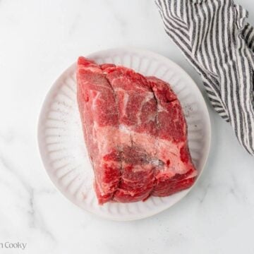 Boneless chuck roast on a white plate with a striped linen on the side.