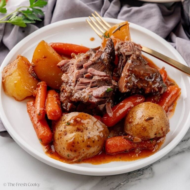 A white plate with pot roast, potatoes and carrots. A gold spoon is resting in the background.