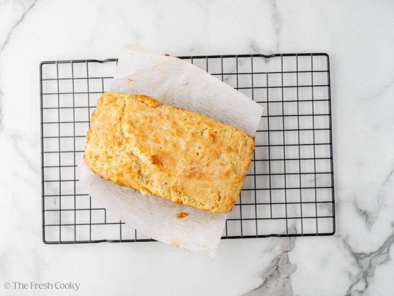 A loaf of no yeast bread cooling on a baking rack with a piece of parchment around it.