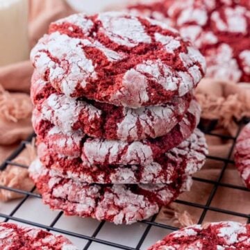 Red velvet crinkle cookies stacked on a wire cooling rack.
