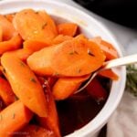 Spoon scooping up some slow cooker glazed carrots from a serving dish.