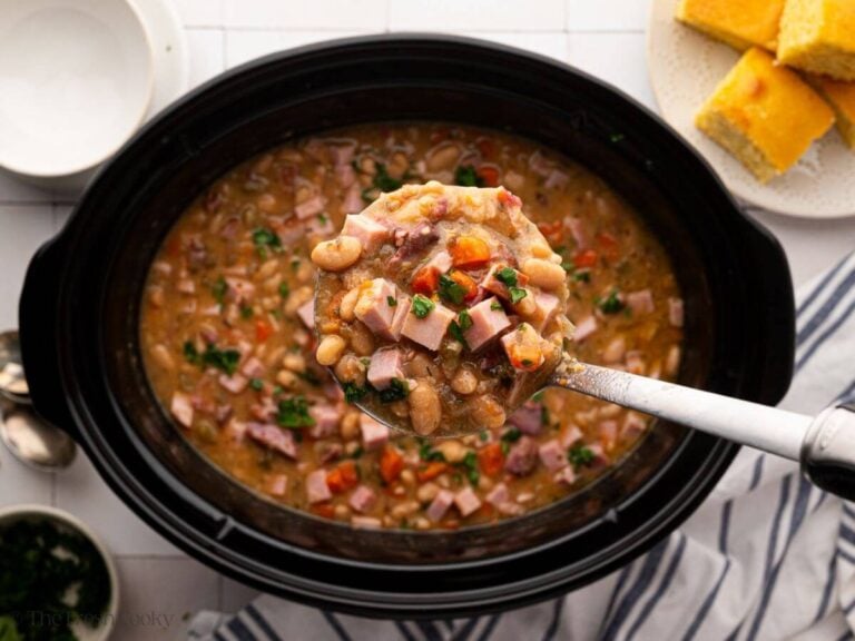 A black slow cooker bowl with a ladle of ham and bean soup.