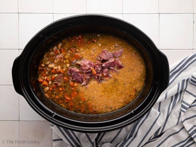 Slow cooker ham and bean soup in a black crock pot bowl with a striped linen.