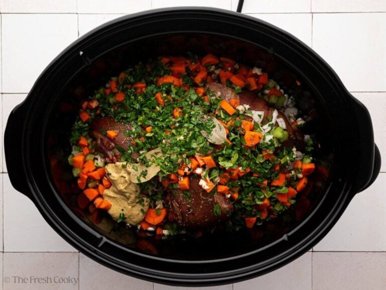 A black slow cooker with ingredients for ham and bean soup.
