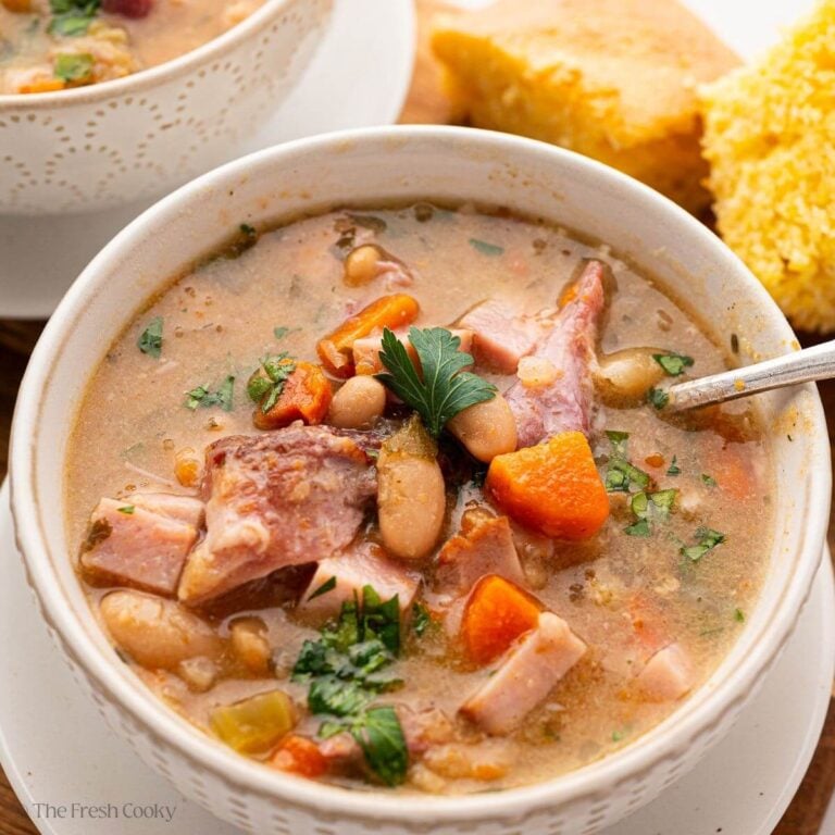 A close up of slow cooker ham and bean soup in a white bowl.