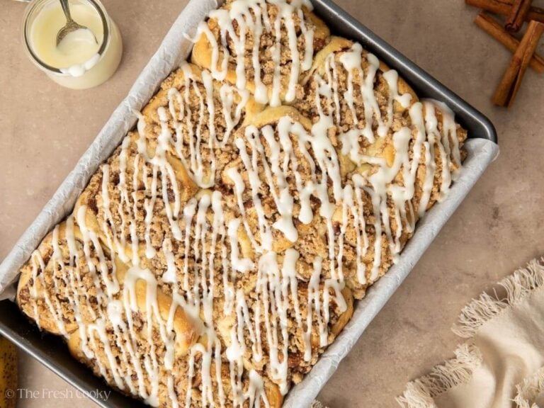 Banana bread cinnamon rolls in pan with cream cheese drizzle on top.
