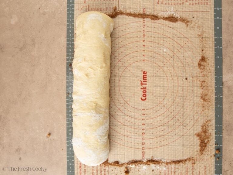 Cinnamon rolls rolled tightly on pastry mat.