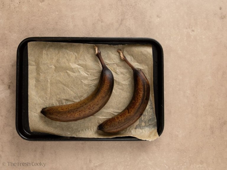 Two dark, roasted bananas on a parchment lined baking sheet.