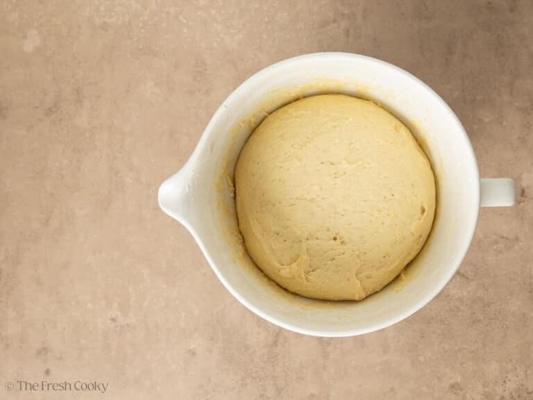 Cinnamon roll dough risen to double in white bowl.