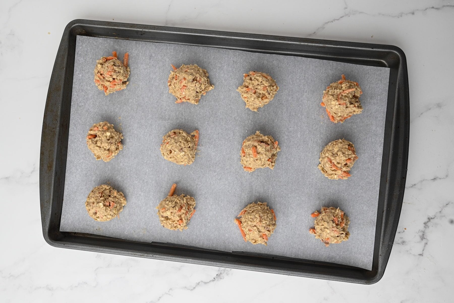 Scooped cookie dough on parchment lined baking sheet.