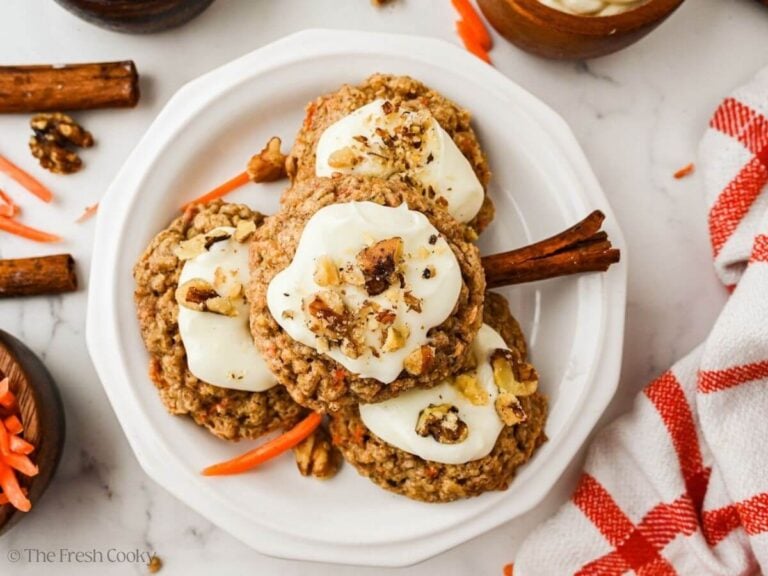 Carrot cake oat cookies frosted and stacked on a pretty scalloped white plate.
