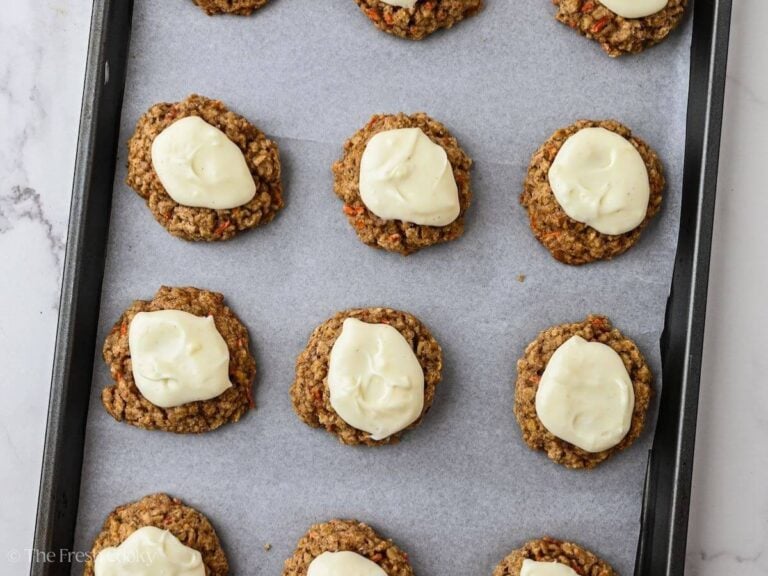Spooning cream cheese glaze onto carrot cake cookies.