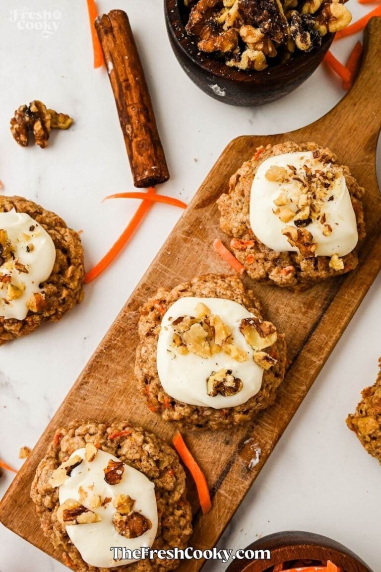 A narrow wooden cutting board with three frosted cookies and one to the side, with a cinnamon stick nearby, to pin.