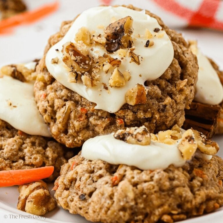 Stacked carrot cake oat cookies topped with a dollop of frosting and chopped walnuts.