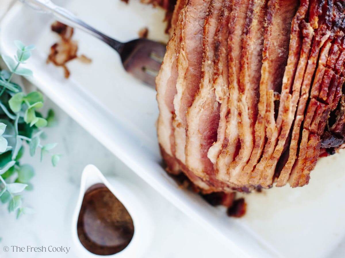 Ham out of the oven on a platter with glaze sauce in pitcher.