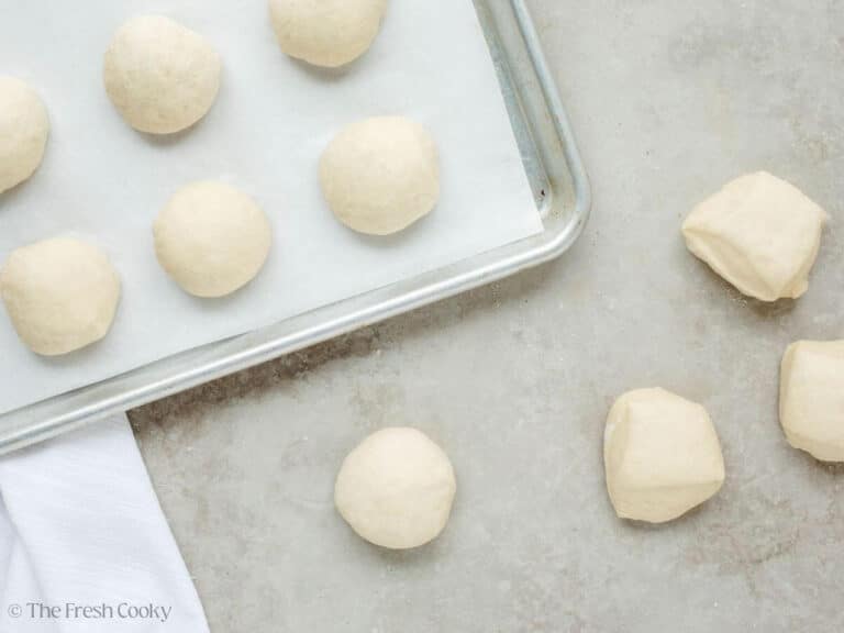 Creating dough balls for rolls and placing them on a parchment lined baking sheet. 