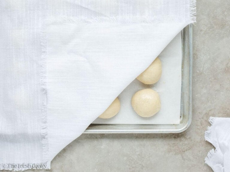 Slightly covered rolls rising on a baking sheet. 