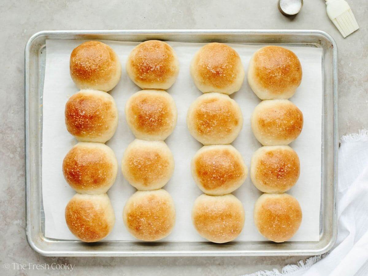 Golden, soft, buttery yeast rolls on a parchment lined baking sheet. 
