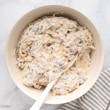 A white bowl with ham and hash brown casserole filling mixed and a white spatula resting on the side.