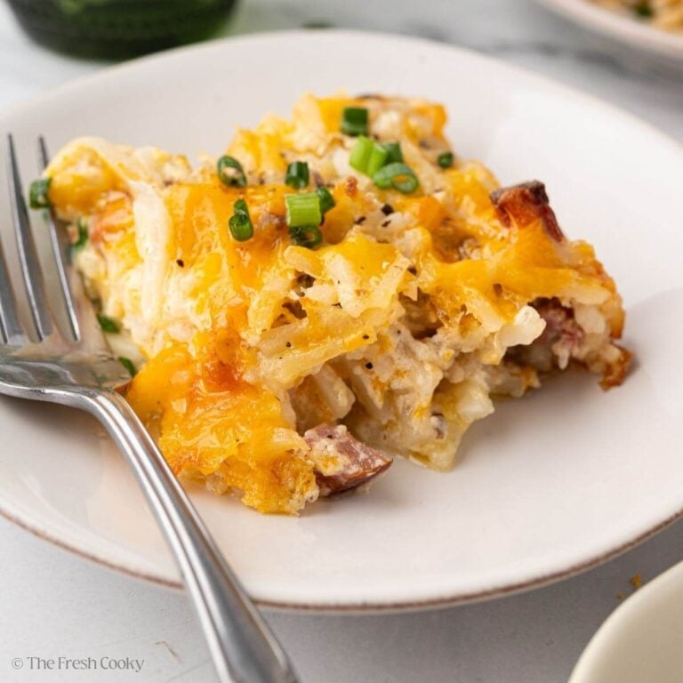A close up image of a serving of ham and hash brown casserole with a fork on the left.
