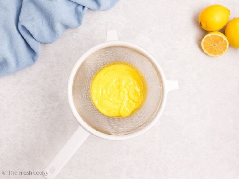 Lemon curd being strained in a fine mesh sieve.