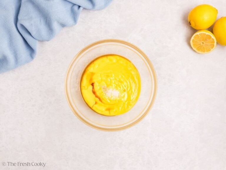 A glass bowl with lemon curd strained, vanilla and salt on top.