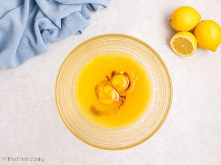 A glass bowl with lemon meringue cupcake wet ingredients including eggs and vanilla extract.