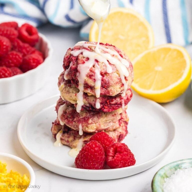 Stack of lemon raspberry cookies with a spoon drizzling glaze over the top.