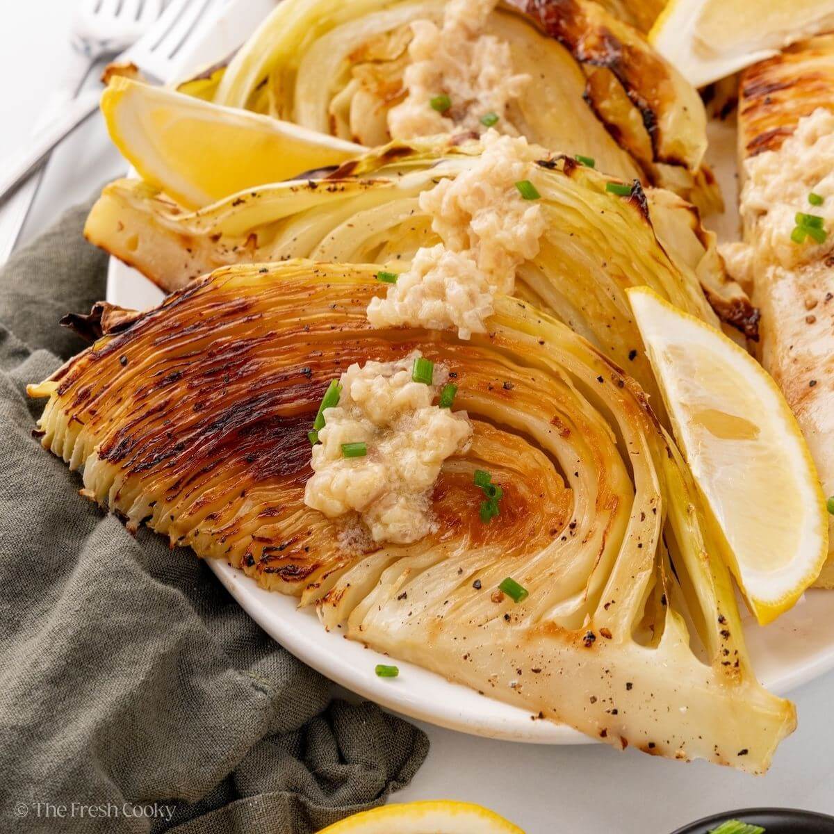 Roasted cabbage wedges leaning on echoner on a platter with sauce on top.