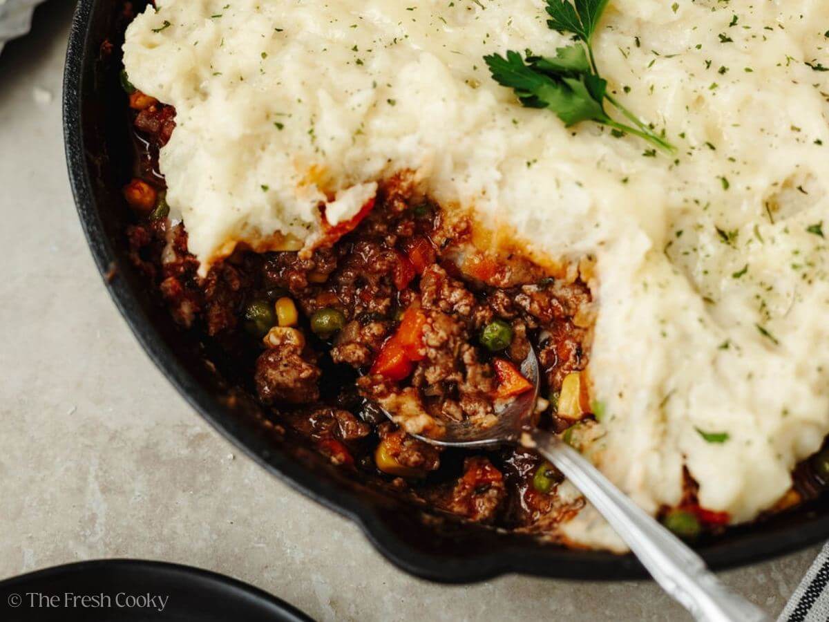 A spoon in a cast iron skillet serving up a meaty, filling of Shepherd's pie. 