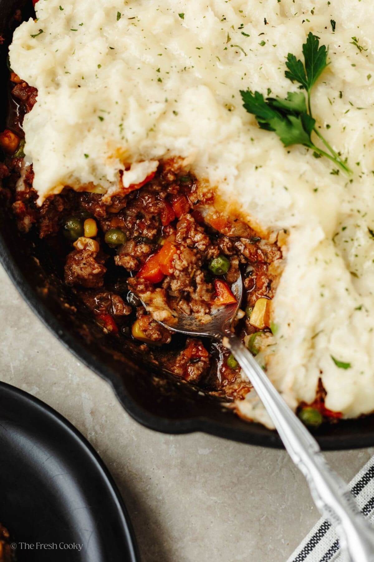 Spooning a portion of Shepherd's pie from a cast iron skillet.