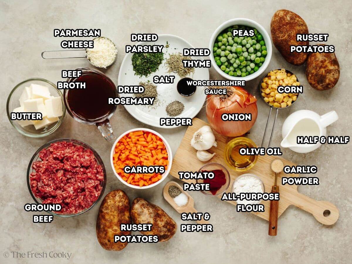 Ingredient shot for Skillet Shepherd's Pie. L-R butter, beef broth, shredded cheese, spices and herbs, peas, frozen corn, Russet potatoes, cream, onion, garlic, oil, flour, Worcestershire sauce, salt & pepper, chopped carrots, and ground beef.