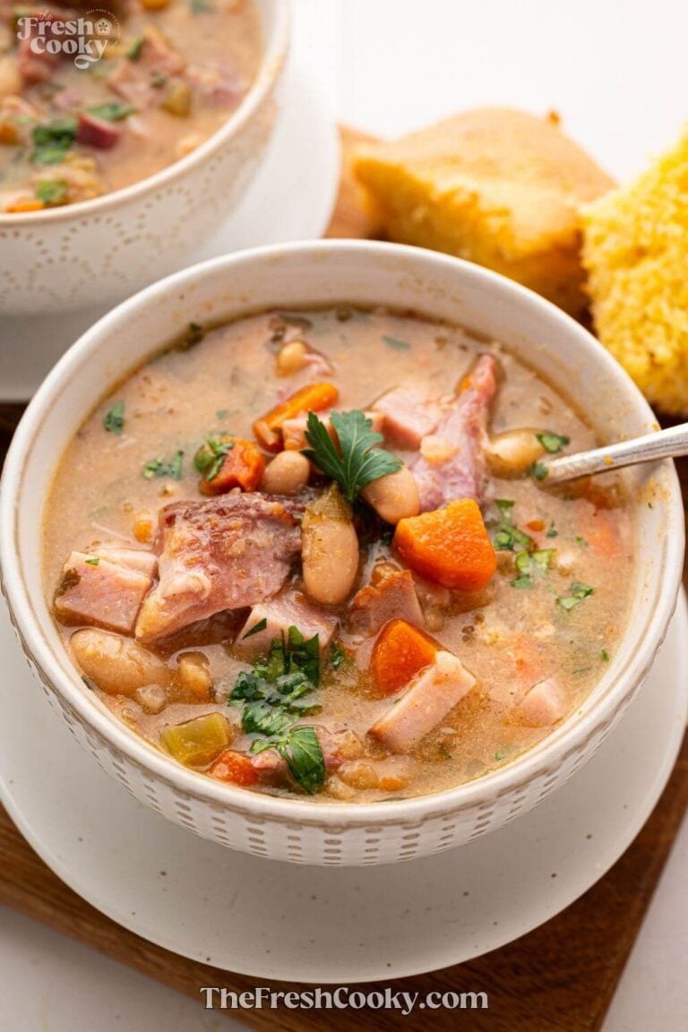 A large bowl of slow cooker ham and bean soup with thick hunks of ham and veggies in a brothy, creamy soup, for pinning.