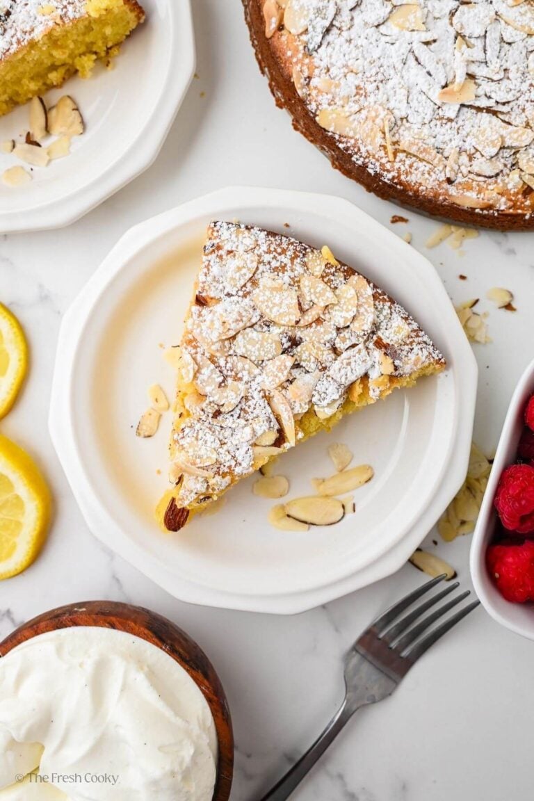 Overhead image of a slice of almond flour olive oil cake with the rest of the cake in the background.