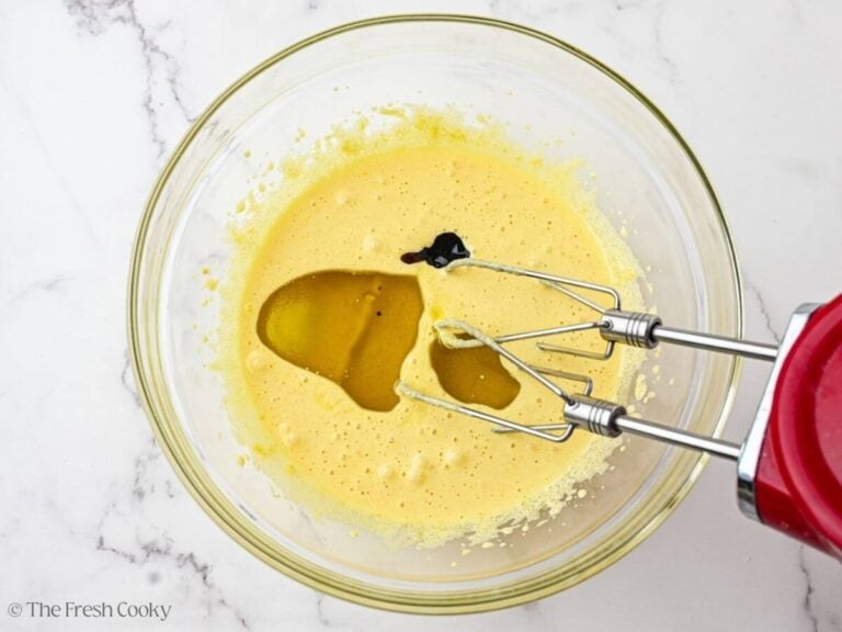 A glass bowl with a hand mixer about to beat the wet ingredients together.