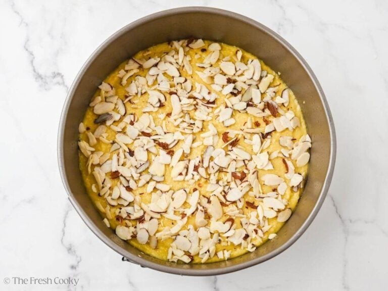 A cake pan with olive oil cake batter and sliced almonds on top.