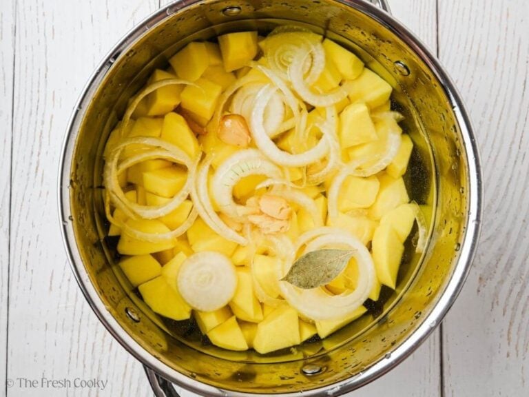 Garlic mashed potatoes with onions, bay leaves, garlic in pot of water.