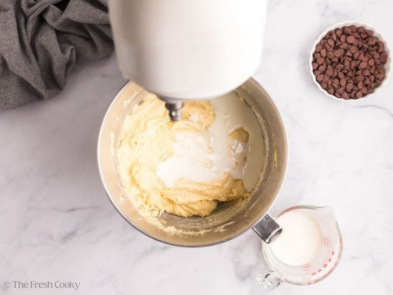 Overhead image of vanilla cake batter with milk added on top. A glass measuring cup with more milk is to the side.