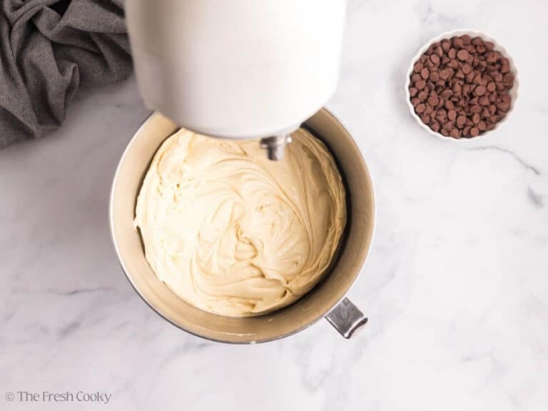 Overhead image of a stand mixer with vanilla cake batter. A white bowl of chocolate chips is to the side.